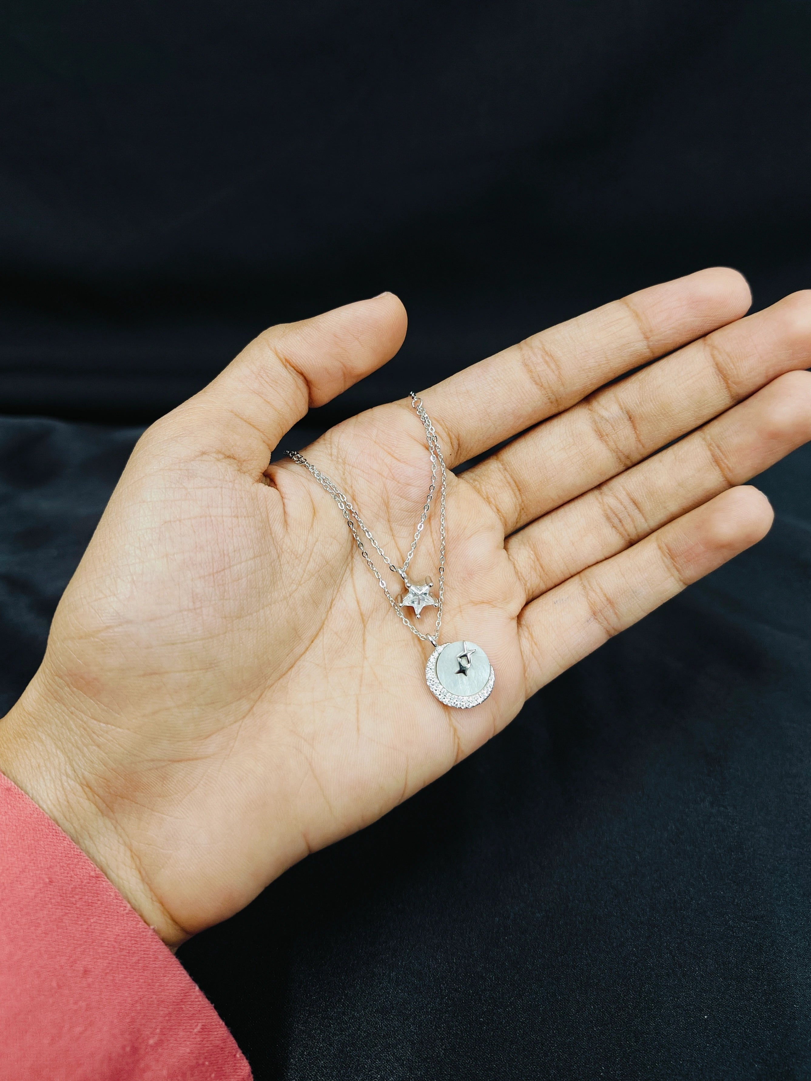Hand holding a silver necklace with star and heart pendants against a dark background